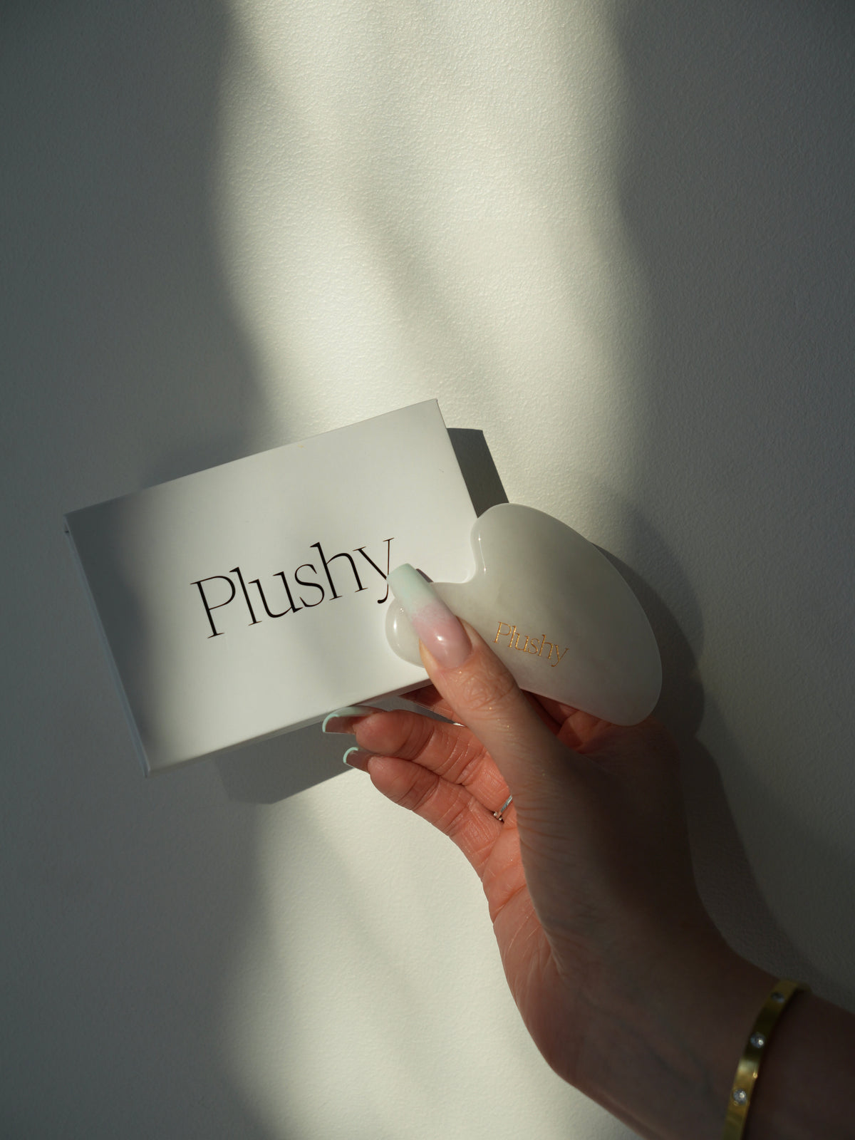 Plushy kinkekarp ja Gua Sha kivi käes päikesevalguses